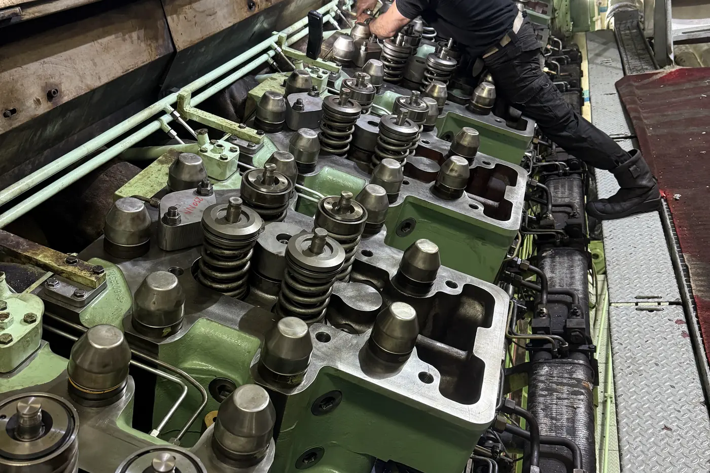 Service engineer working along a row of cylinder heads and valve gear during a marine engine overhaul