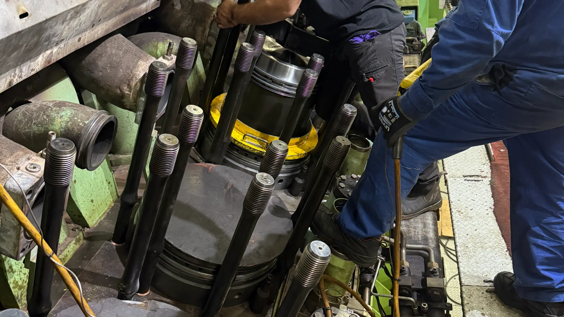 Hydraulic tensioning tools connected to cylinder head studs on a marine engine
